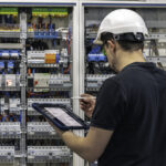 man-electrical-working-switchboard-with-fuses-uses-tablet
